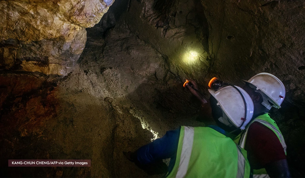 miners in a tunnel with head torchers looking up in a cave