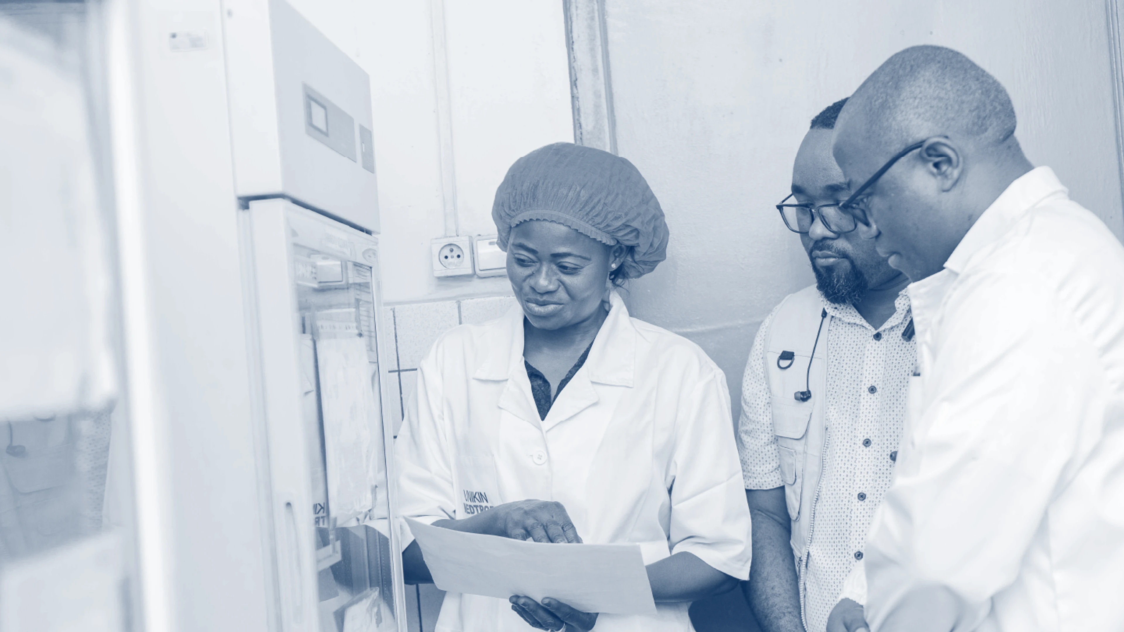 Three researchers from University of Kinshasa looking at paper by lab machine
