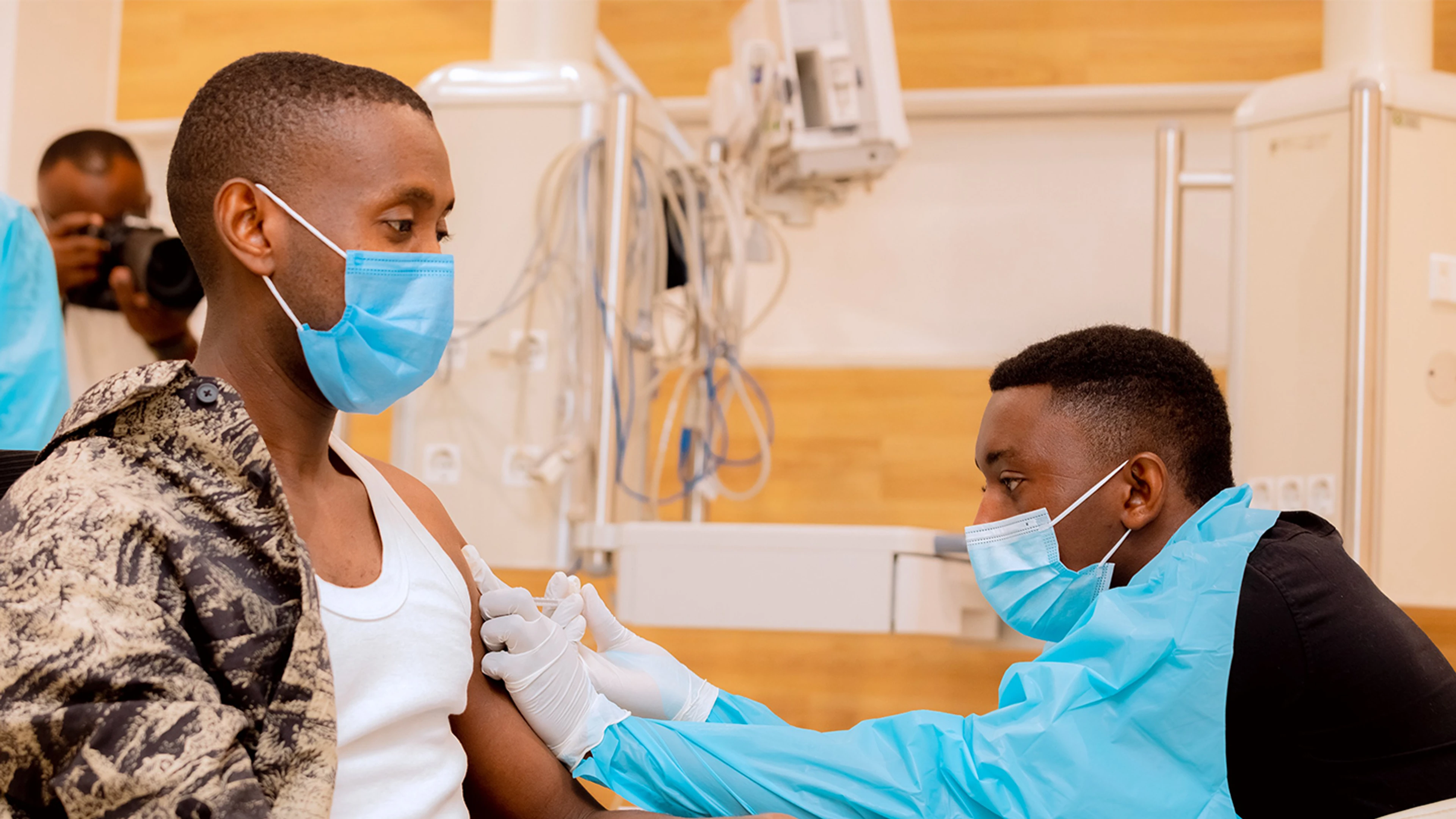 man sat down getting vaccine from health worker in PPE