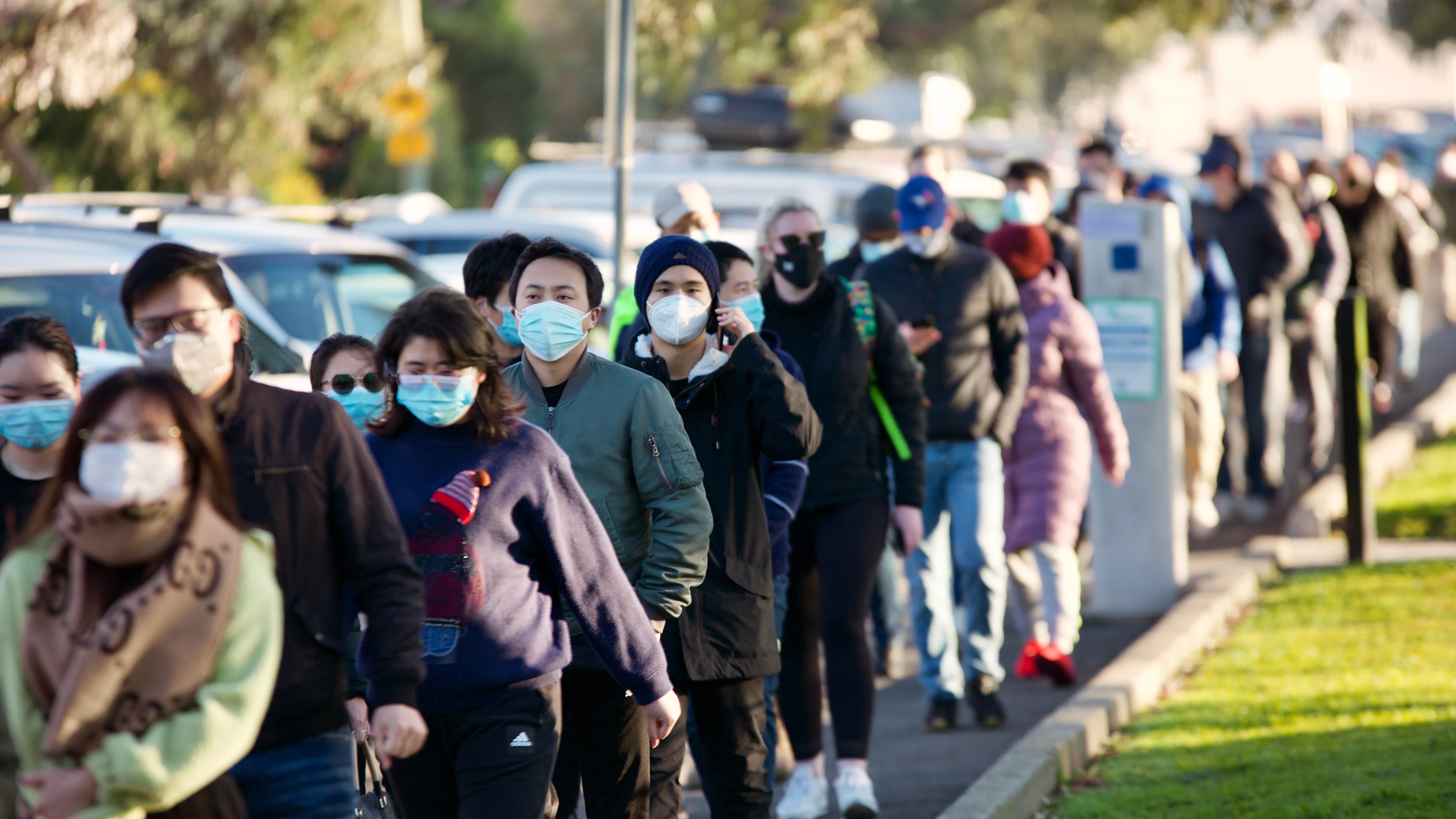 people standing outside in long queue wearing face masks